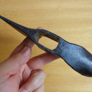 May include: A black metal axe head with a pointed tip and a curved handle. The axe head has a small hole in the center.