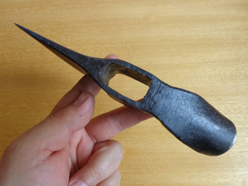 May include: A black metal axe head with a pointed tip and a curved handle. The axe head has a small hole in the center.