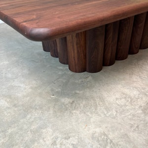 May include: A dark brown wooden coffee table with a rectangular top and a unique base made of stacked, rounded wooden pieces.