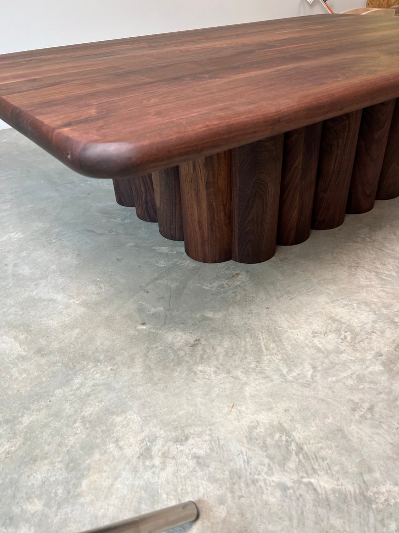 May include: A dark brown wooden coffee table with a rectangular top and a unique base made of stacked, rounded wooden pieces.