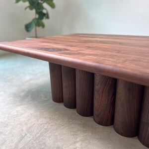 May include: A dark brown wooden coffee table with a rectangular top and a unique base made of stacked cylindrical pieces.