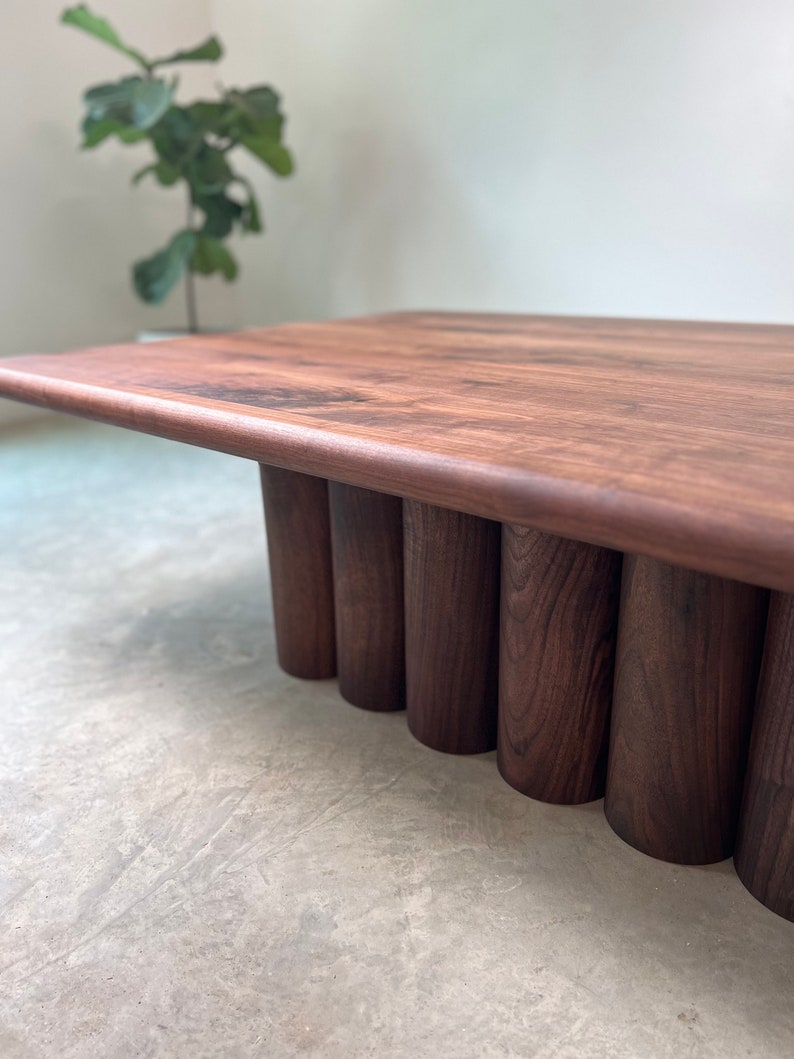 May include: A dark brown wooden coffee table with a rectangular top and a unique base made of stacked cylindrical pieces.