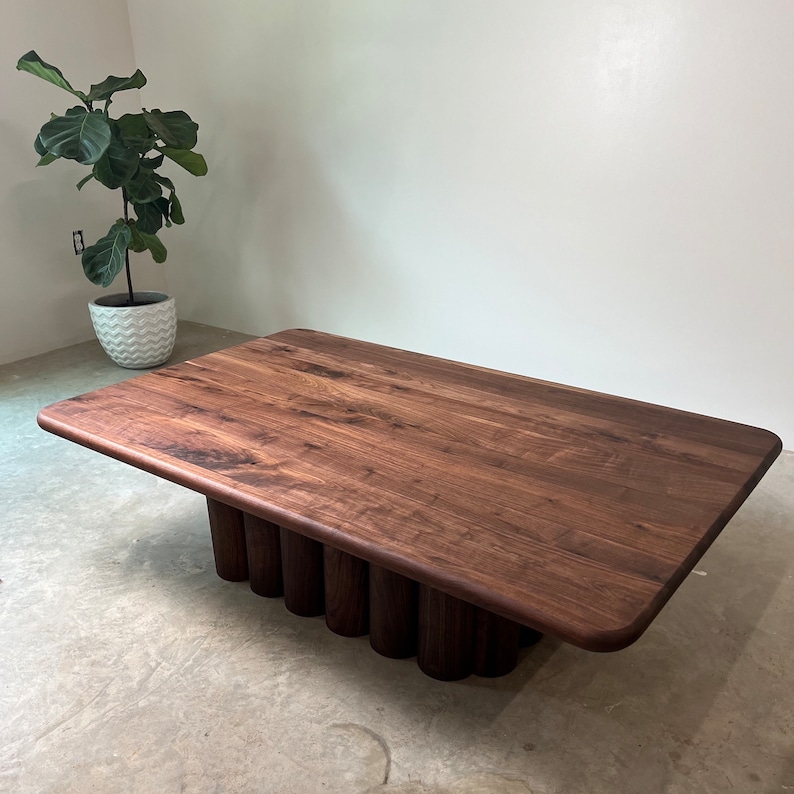 May include: A rectangular coffee table made of dark walnut wood with a unique base design. The base is made of multiple stacked cylinders, creating a visually interesting and modern look.