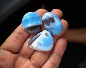 May include: Three blue and black cabochon gemstones with a smooth, polished surface. The stones have a light blue color with black and white patterns.