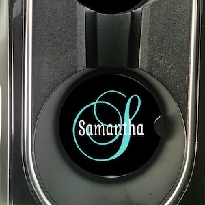 May include: Two black car cup holders with personalised coasters. The coasters are black with a white outline and the name "Samantha" written in a cursive font with a teal blue "S".