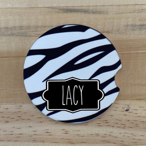 May include: A white and black zebra print car coaster with a black label that says "Lacy" on it.