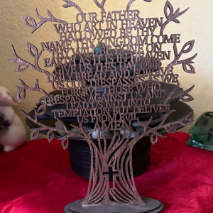 May include: A wooden tree-shaped cutout with the Lord's Prayer carved into the branches. The tree is standing on a wooden base and has a cross at the bottom of the trunk.