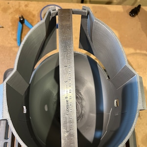 May include: A gray 3D printed helmet with a ruler measuring the inside diameter of the helmet. The ruler measures 25 centimeters.