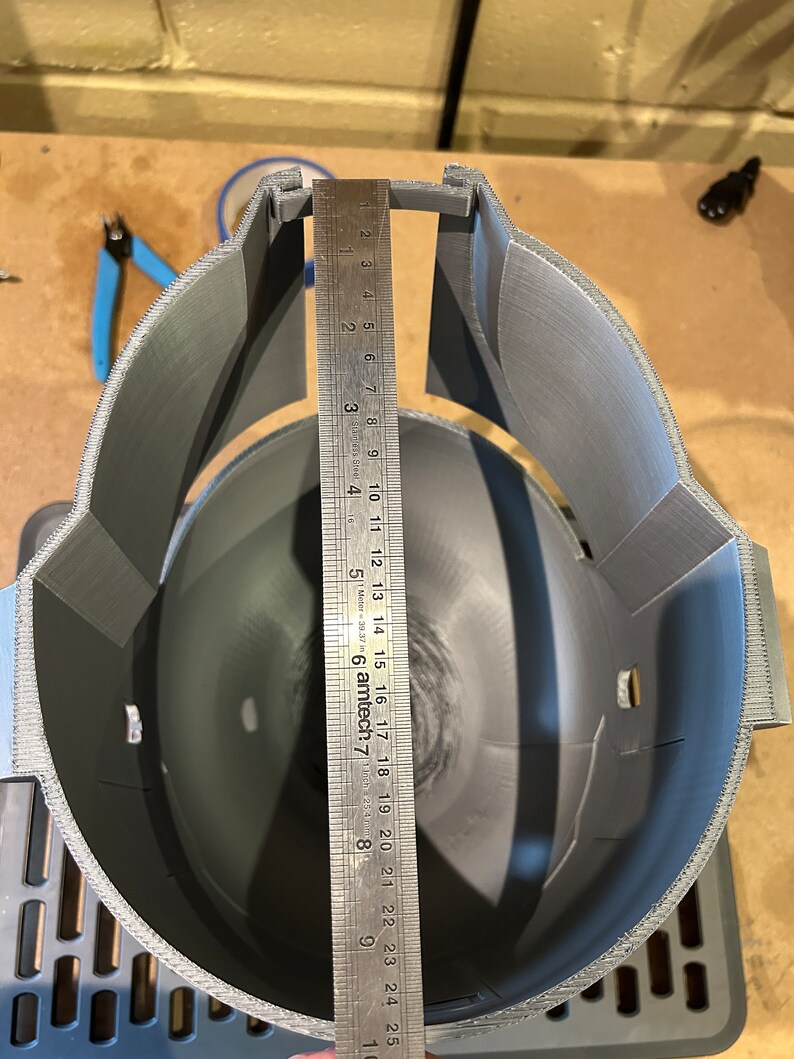 May include: A gray 3D printed helmet with a ruler measuring the inside diameter of the helmet. The ruler measures 25 centimeters.