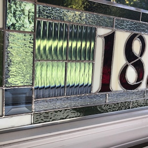 May include: A stained glass house number plaque with the number 1820 in burgundy glass on a white background. The plaque is surrounded by a border of green and gray glass.