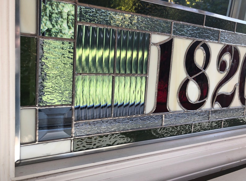 May include: A stained glass house number plaque with the number 1820 in burgundy glass on a white background. The plaque is surrounded by a border of green and gray glass.