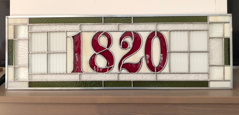 May include: A stained glass window with a white background and a green border. The number 1820 is displayed in red.
