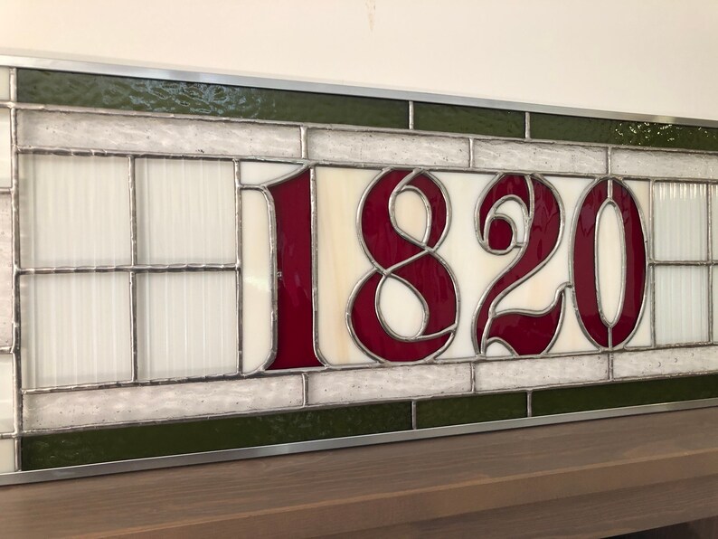 May include: A stained glass window with the number 1820 in burgundy red lettering on a white background. The window is framed in silver and has a green border.