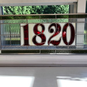 May include: A stained glass house number plaque with the number 1820 in red on a white background. The plaque is surrounded by a border of green and gray glass.