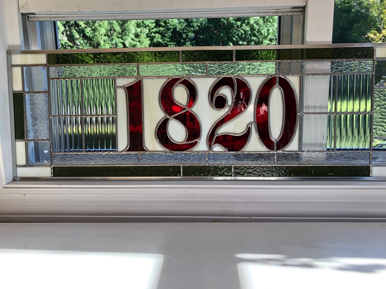 May include: A stained glass house number plaque with the number 1820 in red on a white background. The plaque is surrounded by a border of green and gray glass.
