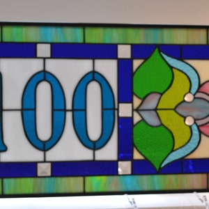 May include: A stained glass window with a blue and white number "100" in the center. The window has a decorative design with green, blue, and pink accents.