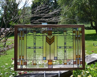 May include: A stained glass window with a geometric design in shades of brown, yellow, and blue. The window is framed in a dark wood frame.