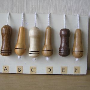 May include: Six wooden light pull chains with different wood grains and colours, labelled A through F. The chains are hanging from a white board.