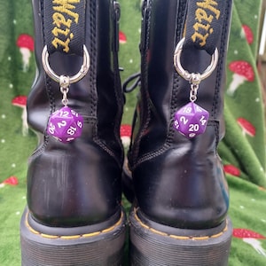 May include: Two black leather platform boots with yellow stitching and a pull tab with "Air Wair" in yellow text. Each boot has a silver charm with a purple, multi-sided die.