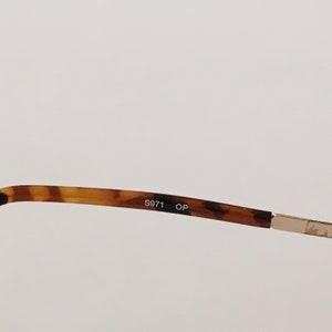 Puede incluir: Primer plano del interior de una montura de gafas de carey con el texto "S971 OP" impreso en negro.