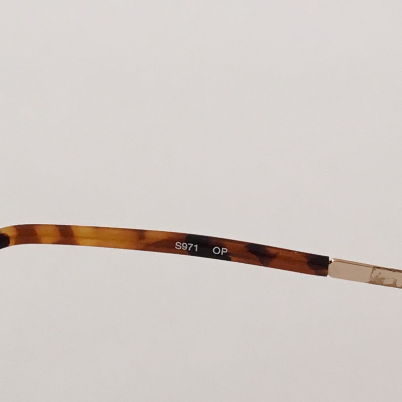 Puede incluir: Primer plano del interior de una montura de gafas de carey con el texto "S971 OP" impreso en negro.