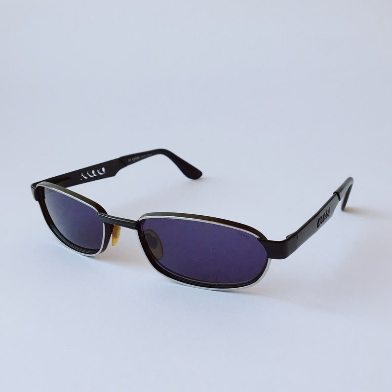 Peut inclure: Lunettes de soleil noires avec une bordure argent&eacute;e autour des verres. Les lunettes portent le logo Gucci sur le c&ocirc;t&eacute;.