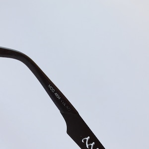 Peut inclure: Gros plan sur la branche noire d'une paire de lunettes avec le texte "MOD. 4984 COL.977" imprim&eacute; sur le c&ocirc;t&eacute;.