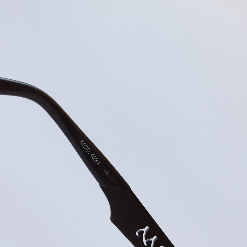 Peut inclure: Gros plan sur la branche noire d'une paire de lunettes avec le texte "MOD. 4984 COL.977" imprim&eacute; sur le c&ocirc;t&eacute;.