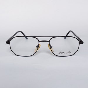 Może przedstawiać: Okulary metalowe w czarnej oprawie z przezroczystymi szkłami. Nazwa marki "Fantasia" jest nadrukowana na prawym szkle.
