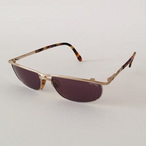 Puede incluir: Gafas de sol de metal dorado con patillas de carey marr&oacute;n y lentes grises oscuras. Las gafas tienen la palabra "COUNTER" impresa en la lente derecha.