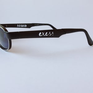 Peut inclure: Lunettes de soleil noires avec une bordure argent&eacute;e et le mot "exess" d&eacute;coup&eacute; dans la monture.