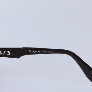 Peut inclure: Gros plan sur la branche en plastique marron d'une paire de lunettes. La branche est marqu&eacute;e "CE - EXESS - MADE IN ITALY".