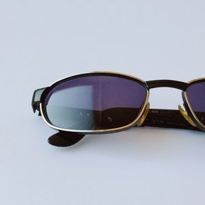 Peut inclure: Lunettes de soleil noires avec une monture argent&eacute;e et des verres fonc&eacute;s. Les lunettes portent l'inscription "EYES" et "MADE IN ITALY" sur la monture.