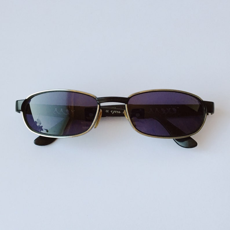 Peut inclure: Lunettes de soleil &agrave; monture noire avec des verres fonc&eacute;s. Les lunettes ont une bordure argent&eacute;e autour des verres.