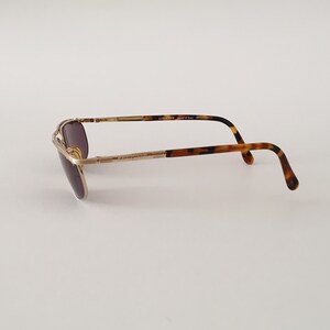 Puede incluir: Gafas de sol aviador doradas con patillas de carey marr&oacute;n. Las gafas tienen una montura de metal y lentes marrones. Las patillas est&aacute;n marcadas con "COOSN'T'N Made in Italy CE".