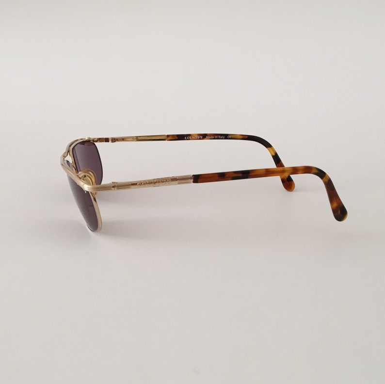 Puede incluir: Gafas de sol aviador doradas con patillas de carey marr&oacute;n. Las gafas tienen una montura de metal y lentes marrones. Las patillas est&aacute;n marcadas con "COOSN'T'N Made in Italy CE".