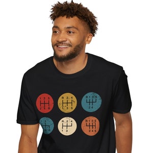 May include: A black t-shirt with a vintage-style graphic of a five-speed manual transmission gear shift pattern. The pattern is repeated five times in different colors: red, blue, yellow, green, and orange.