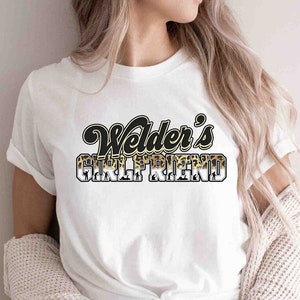 May include: White t-shirt with a black and gold graphic that says "Welder's Girlfriend".