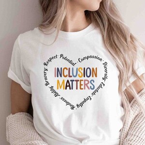 May include: White t-shirt with a heart-shaped design that says "Inclusion Matters" surrounded by the words "Respect, Potential, Compassion, Diversity, Gratitude, Empathy, Kindness, Bravery,  Adult"