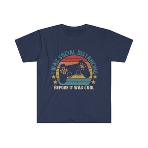 May include: Navy blue t-shirt with a retro-style graphic of a video game controller and the text "I was social distancing before it was cool."