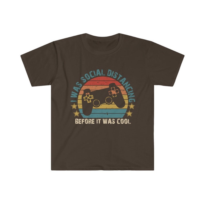 May include: A brown t-shirt with a retro-style graphic of a video game controller and the text "I was social distancing before it was cool."