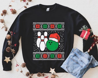 May include: Black long-sleeved sweatshirt with a Christmas-themed bowling design. The design features three bowling pins and a bowling ball wearing a Santa hat. The text "Merry Bowling" is printed on the sweatshirt.