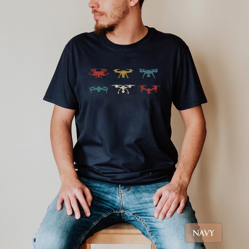 May include: Navy blue t-shirt featuring six drone illustrations in red, yellow, blue, and white. The drones are arranged in two rows of three. The shirt is made of a soft material and is suitable for casual wear.