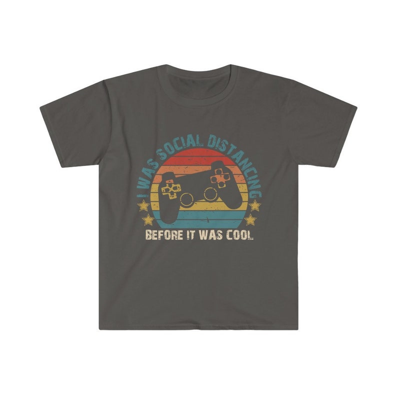 May include: A dark gray t-shirt with a retro-style graphic of a video game controller and the text "I was social distancing before it was cool."