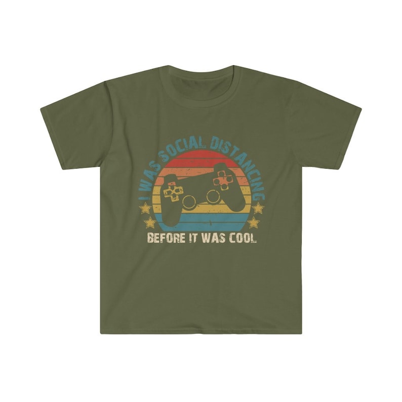 May include: A green t-shirt with a retro-style graphic of a video game controller and a sunset. The text reads "I was social distancing before it was cool."