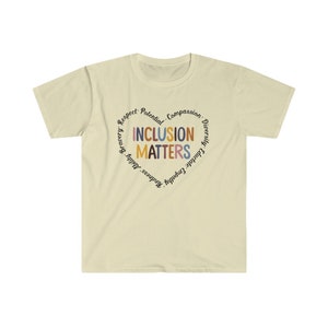 May include: A light beige t-shirt with a circular design featuring the words "Inclusion Matters" in colorful letters surrounded by other words like "Respect, Potential, Compassion, Diversity, Educate, Empathy, Kindness, Bravery,  Adult,  Happiness".