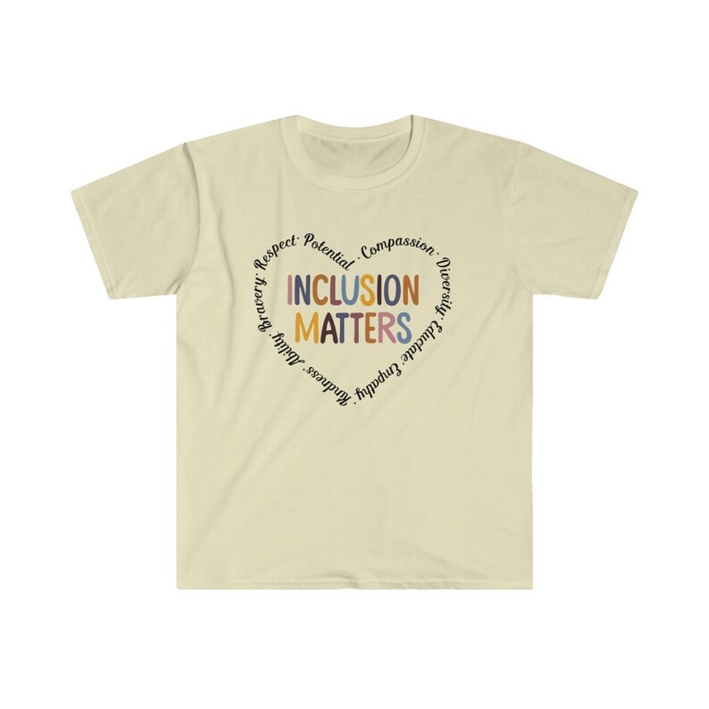 May include: A light beige t-shirt with a circular design featuring the words "Inclusion Matters" in colorful letters surrounded by other words like "Respect, Potential, Compassion, Diversity, Educate, Empathy, Kindness, Bravery,  Adult,  Happiness".