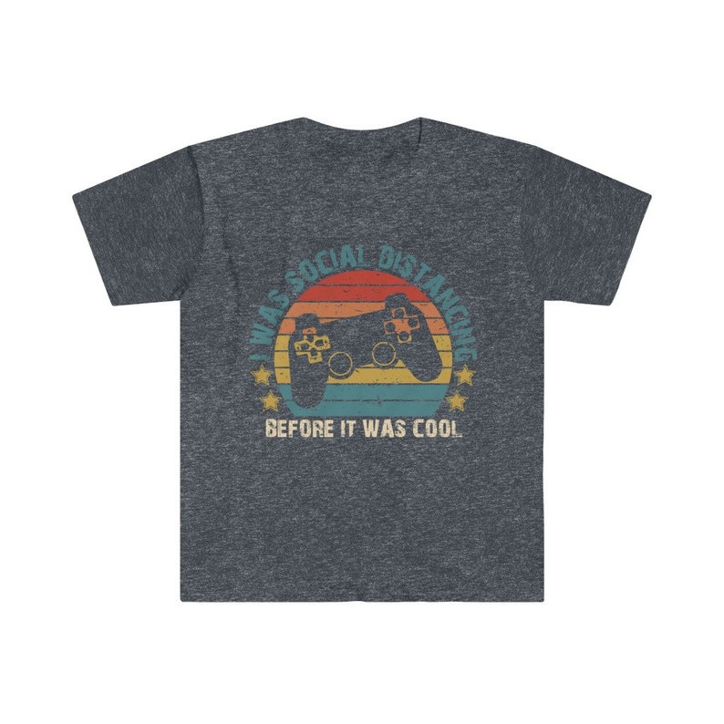 May include: A dark heather grey t-shirt with a retro-style graphic of a video game controller and the text "I was social distancing before it was cool."
