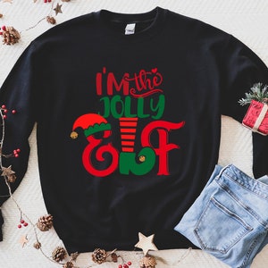 May include: Black Christmas sweatshirt with the text "I'm the Jolly Elf" in red, green, and white. The text is in a festive font and includes a small elf hat.