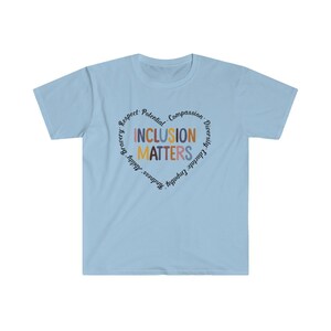 May include: Light blue t-shirt with a circle graphic that says "Inclusion Matters" in colorful letters. The circle is surrounded by the words "Respect, Potential, Compassion, Diversity, Educate, Empathy, Kindness, Bravery,  Adult,  Growth".